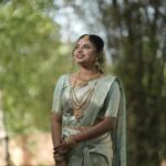 A beautifully dressed Indian woman in a traditional saree, surrounded by greenery, showcasing cultural attire.